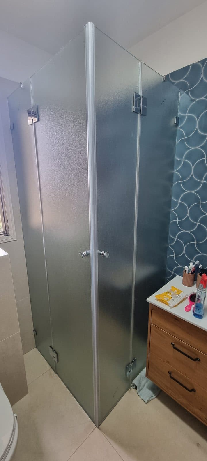 מקלחון פינתי מזכוכית מחוספסת עם צירי כרום וקיר אריחים כחול